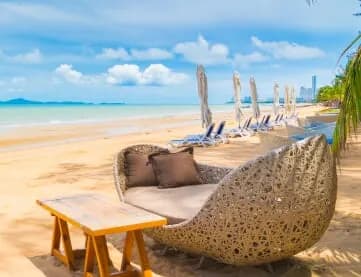 Wicker beach daybed and lounge chairs on a sandy shore